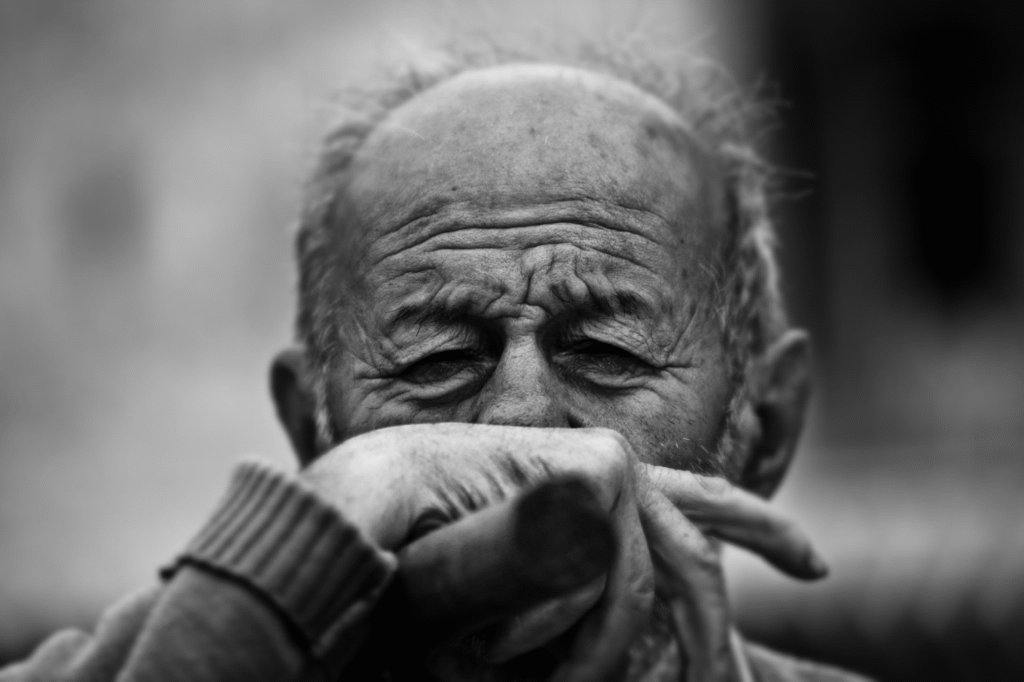 An old person sitting with their face covered.