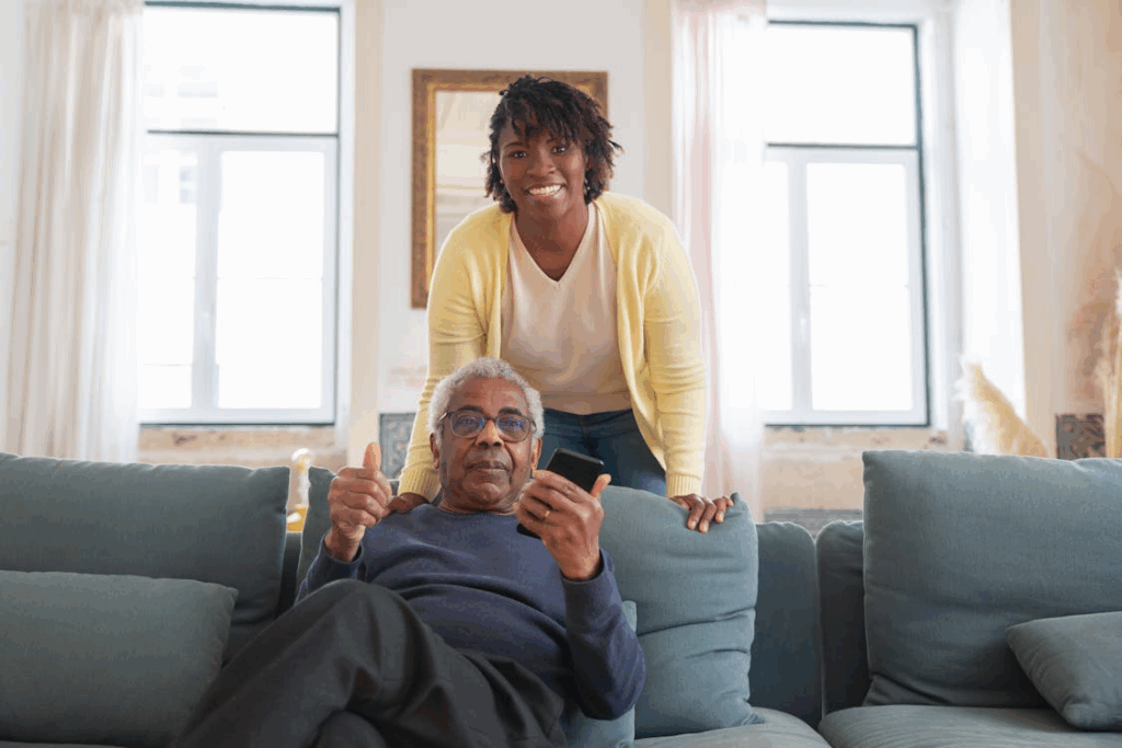 a caregiver smiling while helping an elderly man sit comfortably