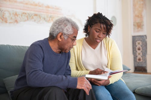 a caregiver assisting an elderly man with reading at home