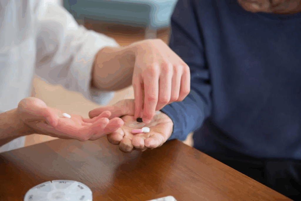 Caregiver placing prescribed pills into an elderly person’s open hand during a daily medication routine at home