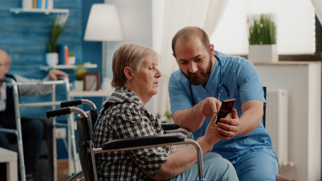 A caregiver showing their phone to an elderly person in a wheelchair