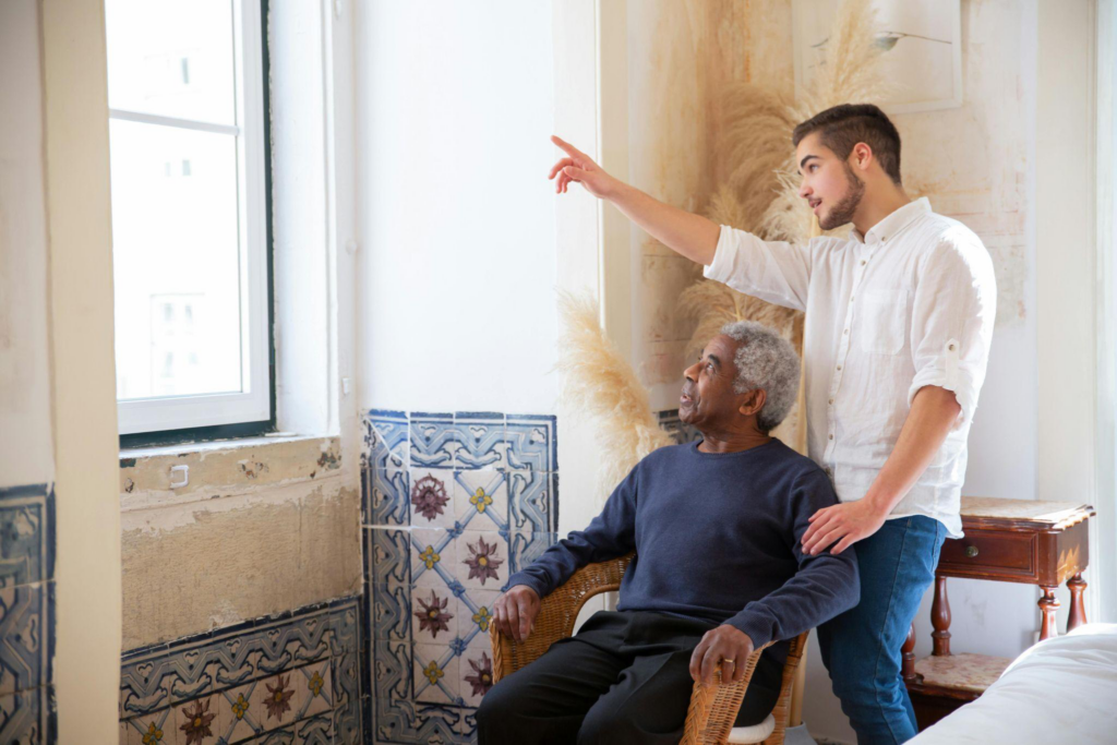 a caregiver and an elderly person looking outside a window