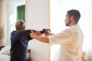 a caregiver and an elderly person exercising in a brightly lit room