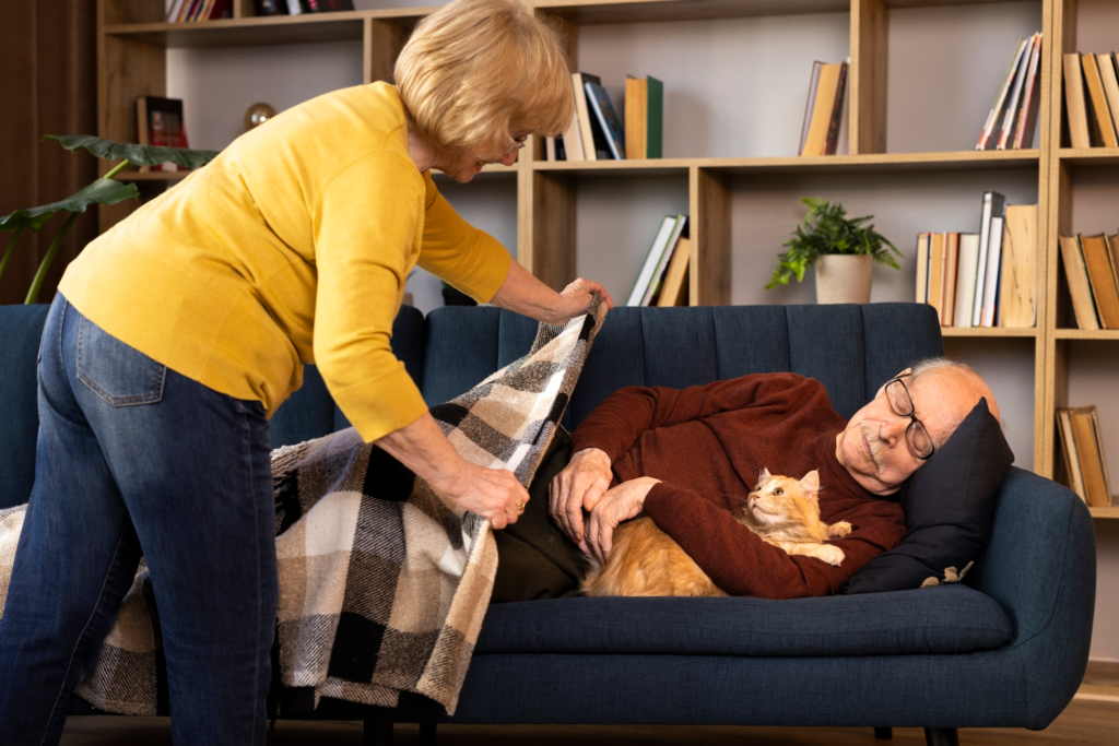 A caregiver putting a blanket on an elderly person napping on a couch