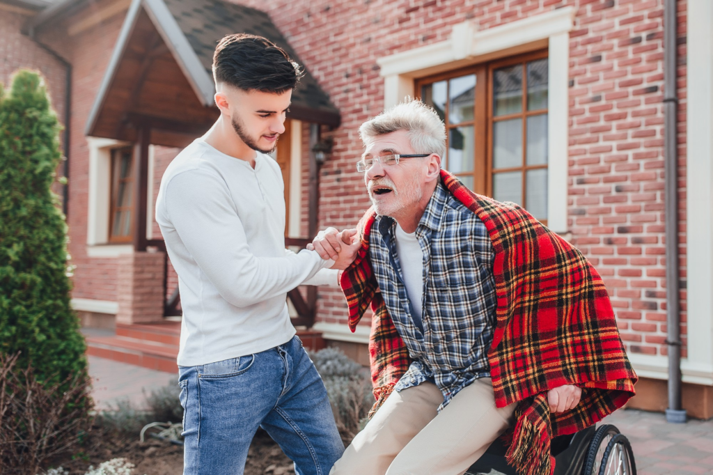 A caregiver helping an elderly man get up from a wheelchair