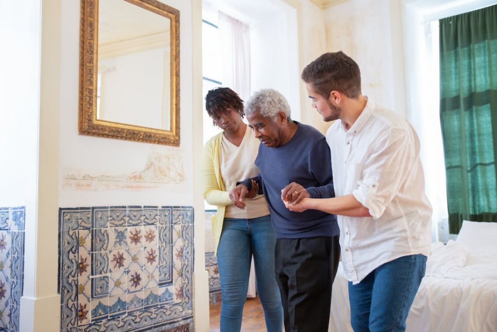 A caregiver assisting an elderly man with walking support inside his home