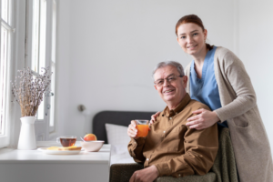 An elderly person holding a juice glass with a caregiver holding their shoulders