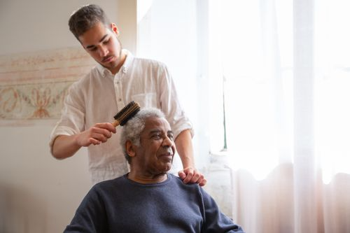 A caregiver combing an old man’s hair