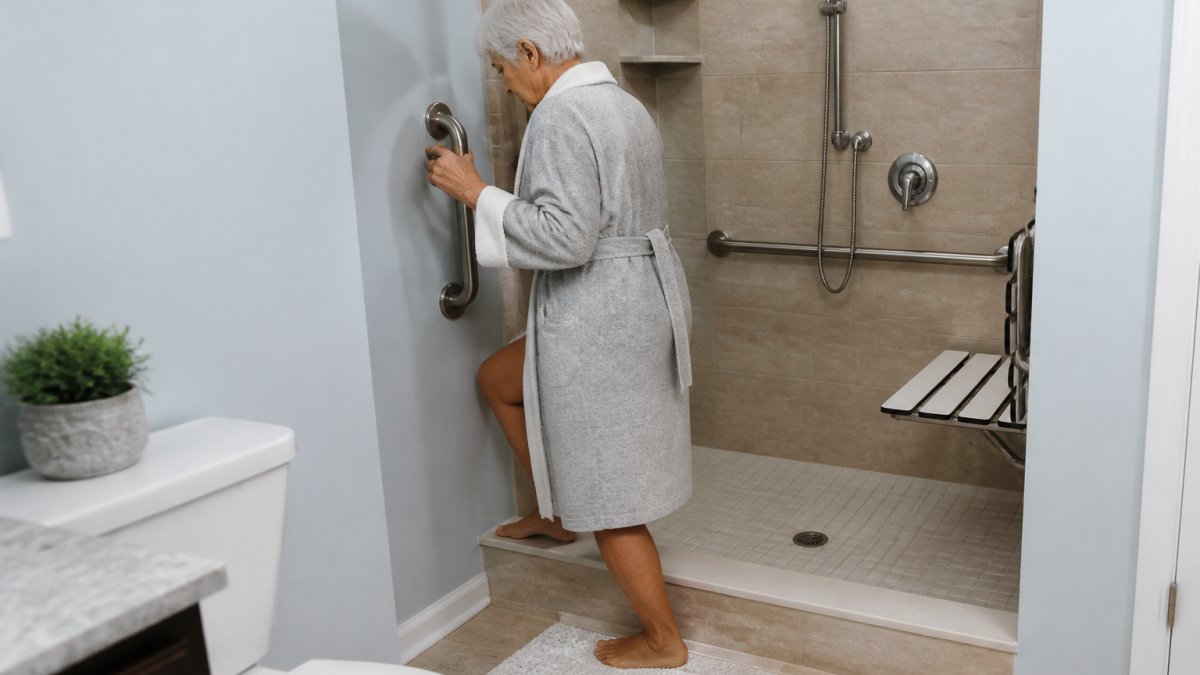 Senior using a grab bar in a bathroom while stepping into a shower, showing proper installation and secure handrail use with non-slip flooring visible